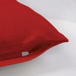Pościel satyna bawełniana 180x200 w kolorze intensywnej czerwieni, widoczna w zbliżeniu na detal zamka błyskawicznego. Produkt leży na gładkim, jasnym tle, odsłaniając matową teksturę materiału. Zamek umieszczony z boku ułatwia wsuwanie poduszki.