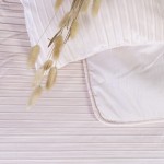Narzuta dwustronna w kolorze beżowym o wymiarach 200x220 cm, z delikatnym, poziomym żłobieniem. Na zdjęciu leży na łóżku, w towarzystwie jasnej poduszki. Widoczna miękka faktura materiału. W tle neutralne, stonowane odcienie.