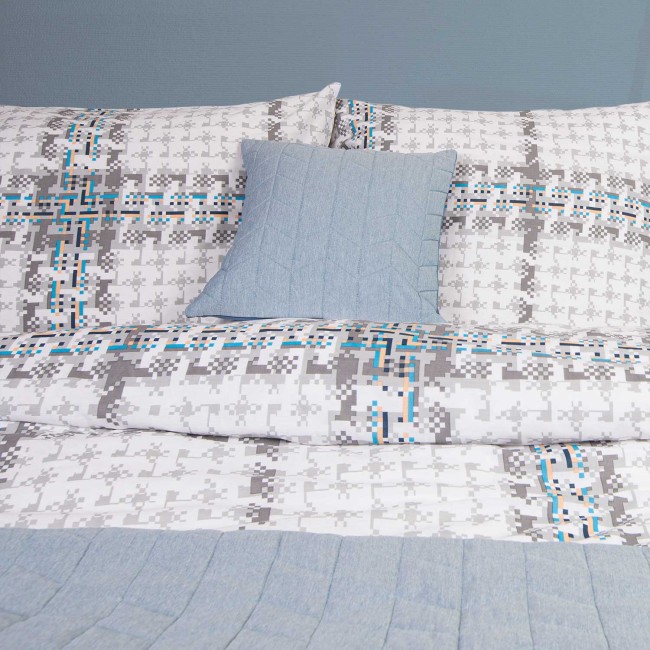 Pościel bawełniana 220x200 Cottonlove w wzór kratki w odcieniach szarości, bieli i niebieskiego. Widoczna poduszka w jednolitym, jasnoniebieskim kolorze. Produkt leży na łóżku, które jest prezentowane na jednolitym tle.