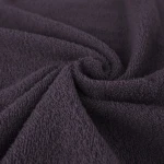 Ręcznik bawełniany 70x140 cm w kolorze fioletowym, leżący na białym tle, z widoczną teksturą w formie pętelkowej. Materiał jest miękki, o gładkim wykończeniu. Ujęcie zbliżeniowe, eksponujące szczegóły splotu i faktury tkaniny.
