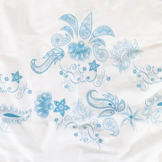 Pościel bawełniana 160x200 Cottonlove w kolorze białym, ozdobiona niebieskim, kwiatowym wzorem. Ukazana z góry, na płasko, ukazując detale nadruku i fakturę materiału. Wzór zawiera stylizowane motywy roślinne i dekoracyjne spirale.