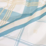 Pościel bawełniana 220x200 Cottonlove w kolorach błękitu i beżu, z wzorem w kratkę. Materiał o gładkiej fakturze, leżący na płaskiej powierzchni. Widoczne różnokolorowe linie i elementy dekoracyjne, podkreślające nowoczesny design.