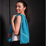Ręcznik sportowy w kolorze błękitnym, o wymiarach 30x110 cm, zawieszony na ramieniu modelki. Z tyłu widoczna kieszonka zamykana na zamek. Wyraźna faktura materiału, zdjęcie na ciemnym tle.