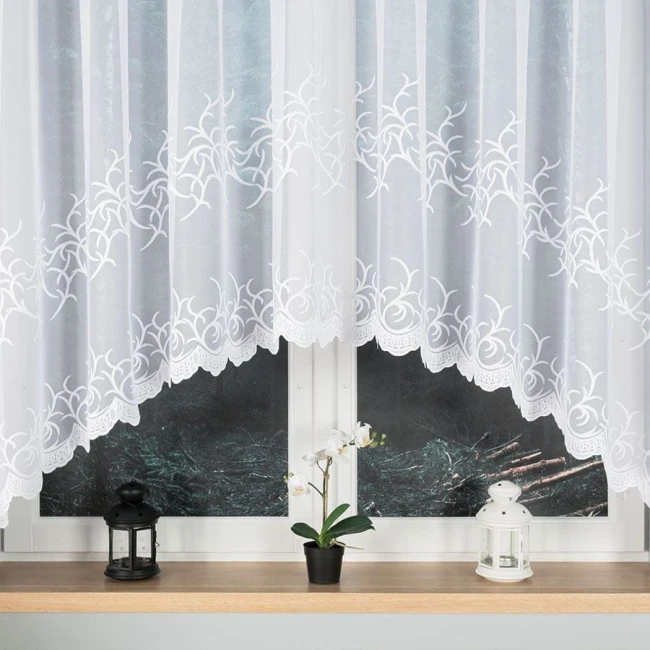 Firana żakardowa Bakaro w kolorze białym, o wymiarach 520x160 cm, zawieszona na oknie. Materiał gładki z haftowanym wzorem roślinnym na dolnej krawędzi. W tle dwa lampiony i doniczka z orchideą na parapecie.