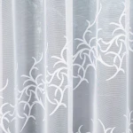 Firana żakardowa Bakaro w kolorze białym, o wymiarach 520x160 cm, z delikatnym, ażurowym wzorem w formie gałązek. Materiał lekki i transparentny, zawieszona w sposób rozłożony, na jednolitym tle.