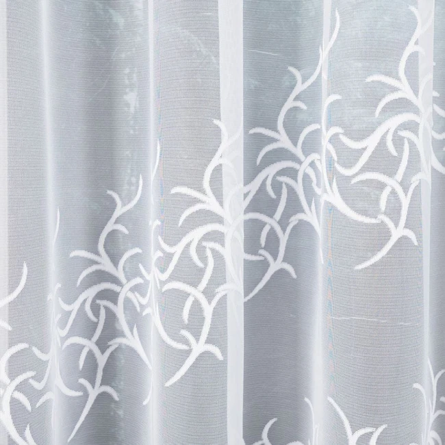Firana żakardowa Bakaro w kolorze białym, o wymiarach 520x160 cm, z delikatnym, ażurowym wzorem w formie gałązek. Materiał lekki i transparentny, zawieszona w sposób rozłożony, na jednolitym tle.
