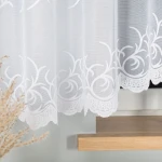 Firana żakardowa, biała, 520x160, wisząca na oknie. Lekka tkanina z delikatnym wzorem roślinnym u dołu. Ujęcie z boku, tło w neutralnym kolorze, drewniana parapet. Zastosowanie w aranżacji wnętrz.