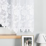Firana żakardowa w kolorze białym, o wymiarach 400x160 cm. Produkt wiszący, z drobnym, kwiatowym wzorem na całej powierzchni. Ujęcie frontalne, zaciągnięta na oknie, obok ramka ze zdjęciem i lampka. Lekka struktura tkaniny, która przepuszcza światło.