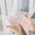 Firana haftowana z delikatnym wzorem na dolnej krawędzi, w kolorze białym. Zbliżenie przedstawia rękę trzymającą fragment firany, podkreślając hafty i falbany. Tło w jasnych odcieniach, co podkreśla właściwości produktu. Wysokość 160 cm.