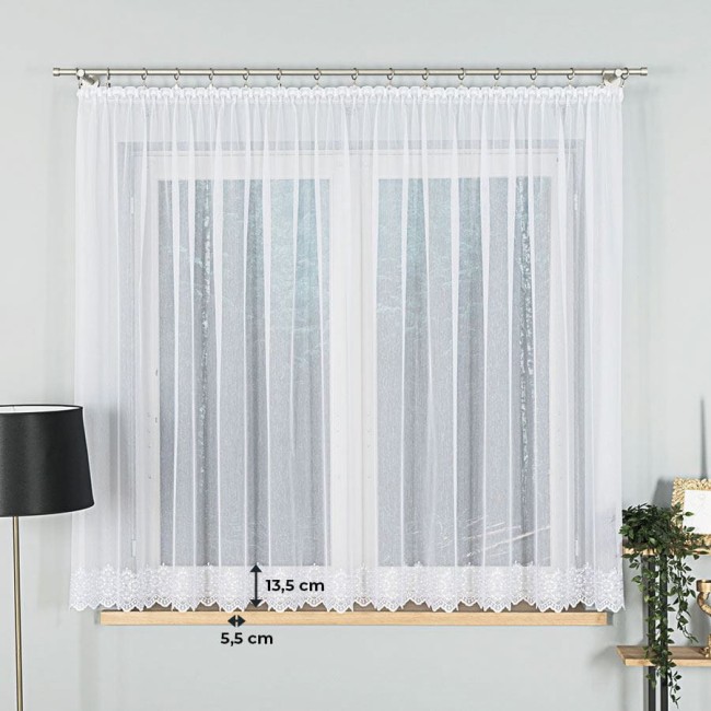 Firana haftowana w kolorze białym, z delikatnym wzorem na dolnej krawędzi, długość 160 cm. Produkt wisi na karniszu, z przodu okna. W tle znajduje się jasna ściana. Widoczne są wymiary: 13,5 cm i 5,5 cm u dołu firany. Brak widocznych napisów lub logo.