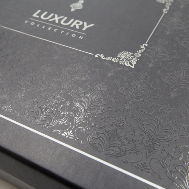 Opakowanie pościeli w kolorze szarym z eleganckim wzorem wytłaczanym. Na froncie widoczne logo LUXURY COLLECTION w białych literach.
