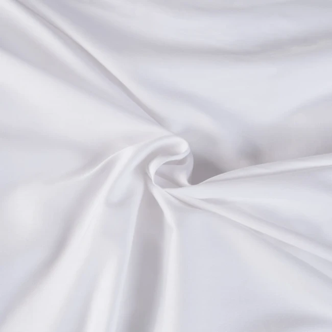 Pościel satyna bawełniana 140x200 w kolorze białym, leżąca na gładkim tle, ukazująca fakturę materiału. Ujęcie w zbliżeniu na szczegóły tkaniny, z widoczną gładkością i połyskiem. Brak dodatkowych wzorów i napisów.