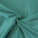 Pościel satyna bawełniana 220x200 w kolorze ciemnego turkusu, leżąca na gładkiej powierzchni. Materiał o gładkiej fakturze, z delikatnym połyskiem. Widoczne złożenia i marszczenia tkaniny, podkreślające jej lekkość. Idealna do aranżacji sypialni.