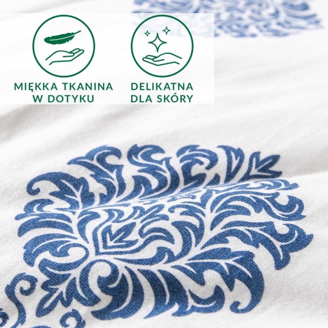 Pościel bawełniana 220x200 z niebieskim ornamentem na białym tle. Materiał jersey, z delikatnym wzorem w stylu roślinnym. Ujęcie w zbliżeniu, eksponujące fakturę tkaniny. Widoczne oznaczenia: miękka tkanina w dotyku i delikatna dla skóry.
