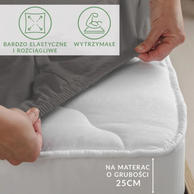 Prześcieradło jersey z elastanem w kolorze antracytowym, rozłożone na materacu o grubości 25 cm. Ujęcie pokazuje elastyczne boki prześcieradła, które idealnie dopasowuje się do materaca. Widoczne napisy informacyjne dotyczące elastyczności i trwałości.