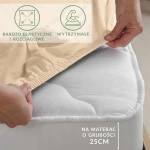 Prześcieradło jersey z elastanem w kolorze beżowym, naciągnięte na materac, widoczne gumki podtrzymujące. Ujęcie z boku, na białym tle.