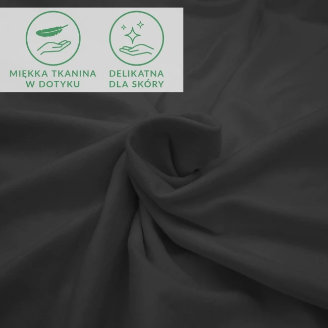 Prześcieradło jersey z elastanem w kolorze czarnym, rozłożone na płaskiej powierzchni. Materiał gładki i elastyczny, lekko zmarszczony. Widoczne ikony informacyjne: miękka tkanina w dotyku oraz delikatna dla skóry.