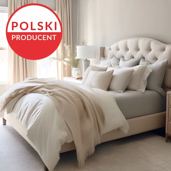 Prześcieradło jersey z elastanem z gumką w odcieniu beżowym, złożone na łóżku. W tle widać elegancką sypialnię z literką do lampy, stoliczkiem nocnym oraz poduszkami w różnych odcieniach beżu i szarości. Tło jasne, z naturalnym światłem.
