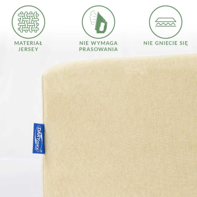 Prześcieradło jersey z gumką w kolorze kremowym, złożone na prosto. Widoczny materiał o gładkiej fakturze, z niebieską metką z logo. Produkt nie wymaga prasowania i nie gniecie się, co potwierdzają ikony na tle.