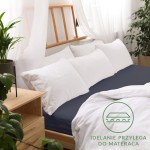 Prześcieradło jersey z gumką 160x200 w kolorze ciemnego granatu, leżące na łóżku. Widoczna gładka struktura materiału, z gumką umożliwiającą dopasowanie do materaca. W tle białe poduszki i osłona łóżka z drewna. W minimalistycznej aranżacji wnętrza.