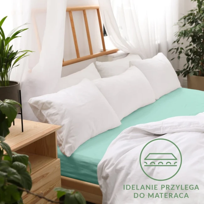 Prześcieradło jersey z gumką 140x200 w kolorze jasnego turkusu, rozłożone na łóżku. Ujęcie z boku, ukazujące gładką fakturę materiału i dobrze przylegające brzegi. W tle widoczne białe poduszki i rośliny, a także drewniana rama łóżka.