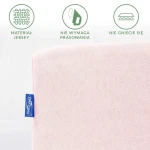 Prześcieradło jersey z gumką w kolorze różu kwarcowego, z widocznym niebieskim logo, leżące na białym tle. Materiał nie wymaga prasowania i nie gniecie się, przyciągający uwagę delikatną fakturą.