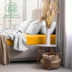 Prześcieradło frotte z gumką 140x200 w intensywnym żółtym kolorze, rozłożone na łóżku. W tle widoczne poduszki w szaro-białym odcieniu oraz dekoracyjny wazon. Ujęcie z boku, na jasnym tle, pokazujące teksturę materiału.