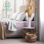 Prześcieradło frotte z gumką 160x200 w kolorze wrzosowym, rozłożone na łóżku z jasnym, gładkim materacem. W tle białe poduszki oraz dekoracyjne elementy jak wazon z suszonymi roślinami, stolik i kosz. Ujęcie frontalne, jasne tło.