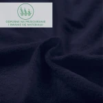 Prześcieradło frotte z gumką w kolorze ciemnego granatu, z bliska, pokazujące teksturowaną powierzchnię materiału. Ujęcie ukazuje fałdy i gładkość, podkreślając elastyczność gumki. Nieczytelny napis o właściwościach materiału w górnej części zdjęcia.