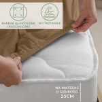Prześcieradło jersey z elastanem w kolorze brązowym, z gumką, widoczne w zbliżeniu. Ułożone na białym materacu o grubości 25 cm, z ręką chwytającą krawędź prześcieradła. Na tle dwa czytelne napisy informacyjne o elastyczności i wytrzymałości materiału.