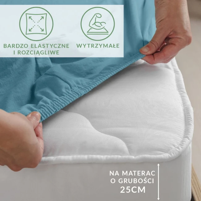 Prześcieradło jersey z elastanem w kolorze błękitnym, rozłożone na materacu, z gumką na bokach. Ujęcie z boku, z widoczną ręką włożoną w materiał.
