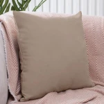 Poszewka dekoracyjna 40x40 cm w ciemno beżowym kolorze, gładka faktura, leżąca na pastelowym kocyku z wzorem. Ujęcie frontalne, produkt położony na kanapie, otoczenie nieco rozmyte, co podkreśla główny element.