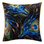Poszewka dekoracyjna w rozmiarze 43x43 cm o czarnym tle z bogatym wzorem pawich piór w odcieniach zieleni, błękitu, różu oraz złota. Produkt leży na płaskiej powierzchni, wykończony żółtym obszyciem.
