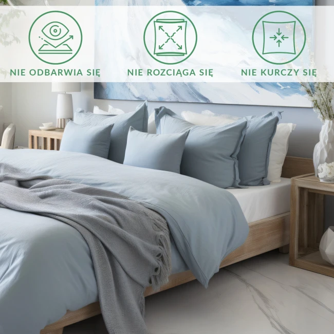 Prześcieradło satynowe bez gumki 200x220 w kolorze kremowym, leżące na łóżku. W tle poduszki w odcieniach błękitu oraz szary koc z frędzlami.