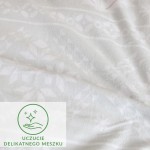 Flanelowa pościel w kolorze białym, z delikatnym wzorem w kształcie liści i kwiatów. Materiał o matowej fakturze, leżący na płaskiej powierzchni. Na tkaninie umieszczona zielona grafika z tekstem „Uczucie Delikatnego Meszku”.