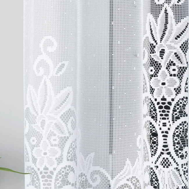 Firana żakardowa Berenika w kolorze białym o wymiarach 300x160 cm, zawieszona w pionie, z delikatnym, koronkowym wzorem. Tło proste, na jasnym, neutralnym tle, podkreślającym detale faktury i wzorów.