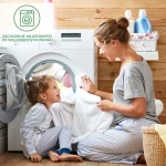 Mama w szarym t-shircie i dziecko w niebieskich piżamach przy pralce. Dziecko siedzi na podłodze i się uśmiecha, mama trzyma białą ręcznikową tkaninę.