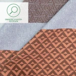 Pościel satyna bawełniana 160x200 Exclusive Mia w pomarańczowo-brązowe pasy. Widoczne różne wzory geometryczne na materiałach. Pozycja leżąca, tło proste. Gładka i teksturowana faktura tkaniny.