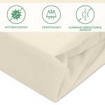 Ochronne prześcieradło z gumką w kolorze kremowym o wymiarach 60x120 cm, leżące złożone. Materiał o teksturze bawełny, widoczne zakładki. Elementy na górze przedstawiają właściwości: antybakteryjny, oddychający, eliminuje nieprzyjemne zapachy.
