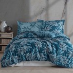 Pościel satyna bawełniana 220x200 w odcieniu błękitnym z delikatnym wzorem liści. Produkt leży rozłożony na łóżku, z dwoma poduszkami w tle. Tło neutralne, z dekoracyjnymi naczyniami obok. Tekstura materiału gładka i błyszcząca.