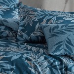 Pościel satyna bawełniana 160x200 Luxury Premium Irene w odcieniach niebieskiego z delikatnymi liśćmi. Ułożona poziomo, z poduszkami w różnych rozmiarach. Tło neutralne, tekstura materiału widoczna. Wzór liści w jasnych kolorach, delikatne detale.