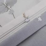 Pościel satyna bawełniana 220x200 Luxury Premium Perimelis w biało-szare delikatne kwiaty, z widocznym zamkiem błyskawicznym. Ujęcie z góry, ukazujące teksturę tkaniny oraz detale wzoru. Kolory stonowane, z kwiatowym motywem na jasnym tle.