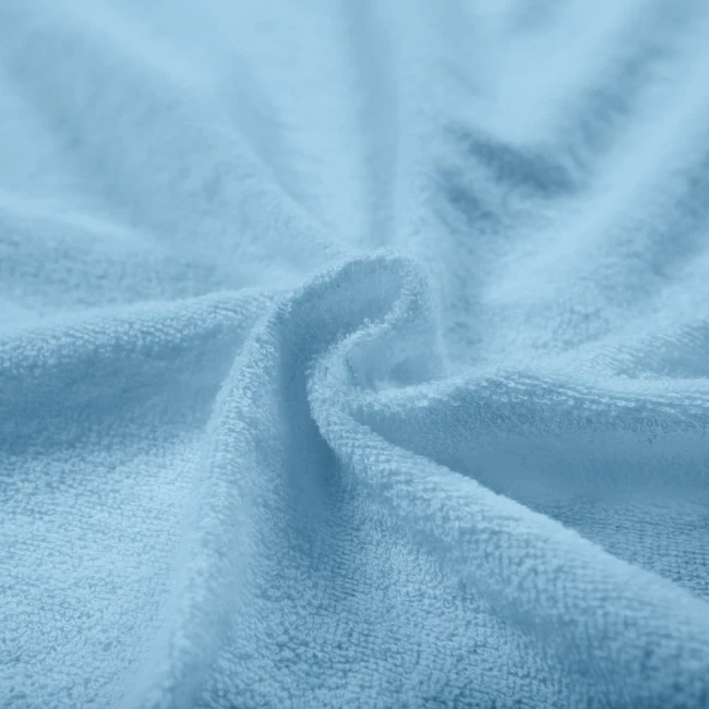 Poszewka frotte 40x40 w odcieniu błękitu. Zbliżenie na miękką, teksturowaną powierzchnię materiału. Widoczny jest drobny splot włókien, wodnisty kolor oraz lekko falująca struktura. Produkt leży na gładkiej powierzchni.