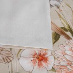Pościel bawełniana 200x220 Cottonlove Exclusive Sidelya w beżowe kwiaty, złożona na jasnym tle. Widoczny fragment poszewki w białym kolorze, z subtelną teksturą. Kwiaty w odcieniach różu i zieleni, delikatny wzór na tle beżu.