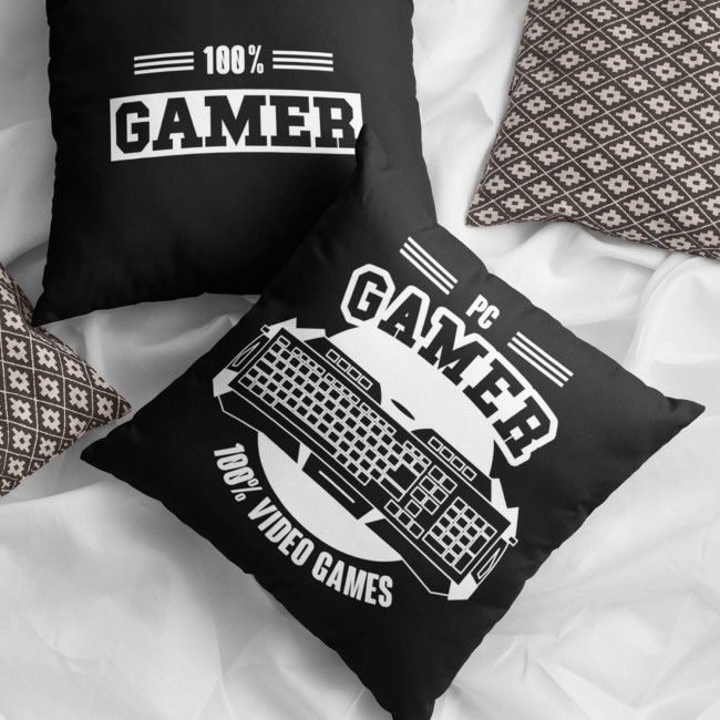 Poduszka 40x40 cm w kolorze czarnym z białym nadrukiem 100% GAMER i motywem klawiatury. Ułożona na jasnym podłożu obok wzorzystej poduszki, ukazana z góry, z wyraźnymi detalami nadruku oraz teksturą materiału.