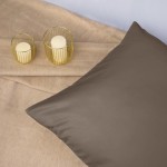 Poszewka satynowa 50x70 w kolorze sepia leży na jasnym tle, obok dwóch świec w złotych, drucianych osłonkach. Materiał jest gładki i błyszczący, a kształt poszewki prostokątny. Ujęcie jest z góry, ukazujące detale tkaniny.