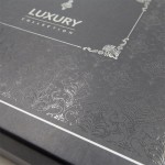 Połyskujące opakowanie pościeli w kolorze ciemnoszarym z dekoracyjnym tłoczeniem i białymi detalami, widok z góry. Na pokrywce umieszczono napis LUXURY COLLECTION. Wzór na opakowaniu przedstawia zdobienia roślinne, nadając elegancki charakter.