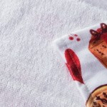 Ścierka kuchenna w białym kolorze z zielonymi elementami świątecznymi. Ujęcie z bliska ukazuje fragment wzoru z motywami bożonarodzeniowymi, takimi jak czerwone serca i prezenty. Materiał jest teksturowany, a rozmiar to 38x60 cm.