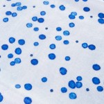 Ścierka kuchenna Ocean Blue w białym kolorze z niebieskimi plamkami w różnych odcieniach. Ułożona w poziomie, z teksturą materiału wyczuwalną w detalu. Wymiary 38x60 cm, idealna do użytku w kuchni.
