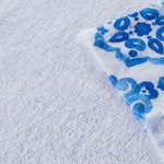 Ścierka kuchenna Ocean Blue w kompletach 2 sztuk, wymiary 38x60 cm. Biała z niebieskim wzorem o fakturze frotte. Widok z góry, zwinięta. Łatwe w użyciu w kuchni, idealne do codziennych czynności. Stonowane tło podkreśla wzór.